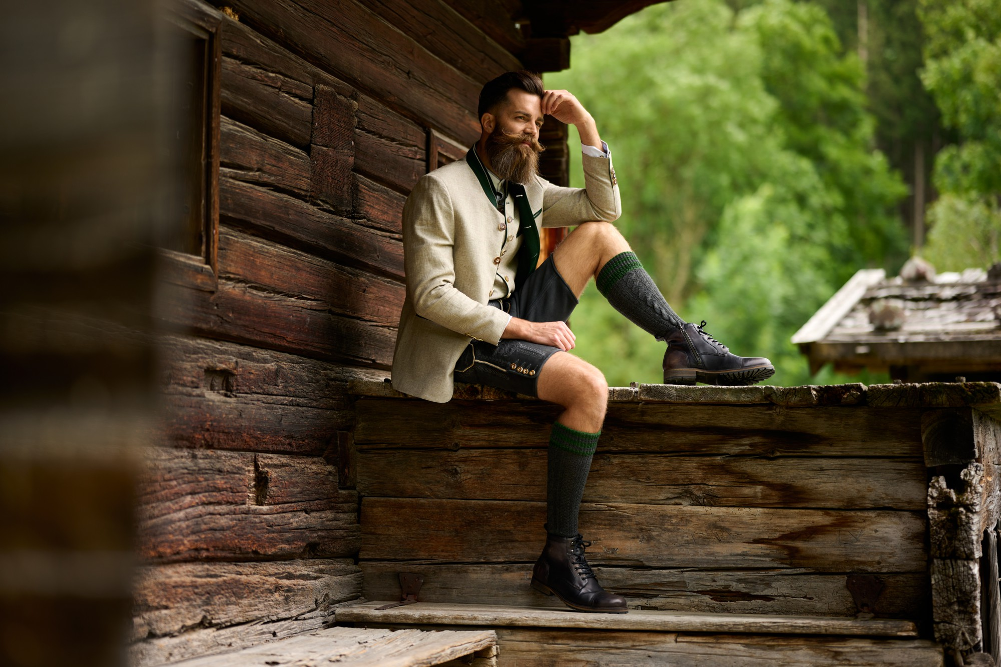 Mann in Tracht sitzt vor einem alten Bauernhof